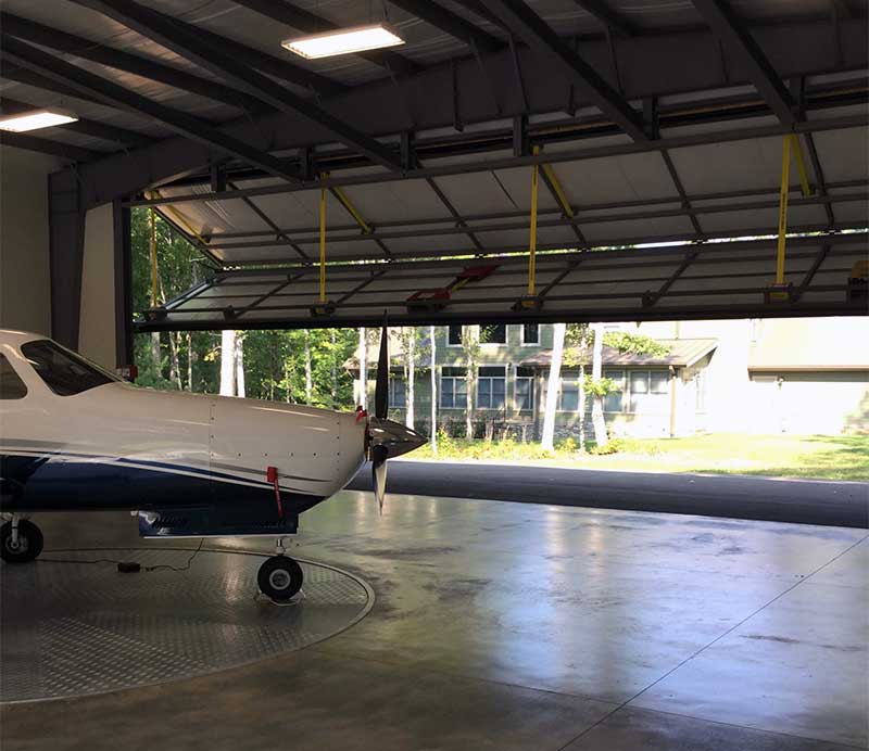 Two big 48 x 15-foot Schweiss bifold liftstrap/autolatch doors open on both ends of the hangar. The front of his Piper Malibu Matrix is shown on the remote controlled carousel that allows him to rotate the plane for easy exit.